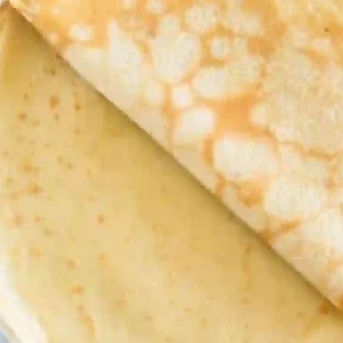A stack of thin, golden crepes with one crepe partially folded over on top.