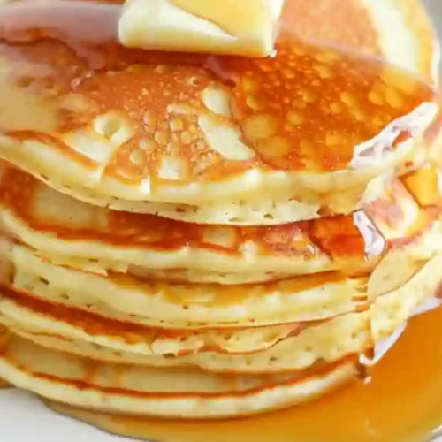 A stack of fluffy pancakes topped with a pat of butter and drizzled with syrup, served on a white plate.