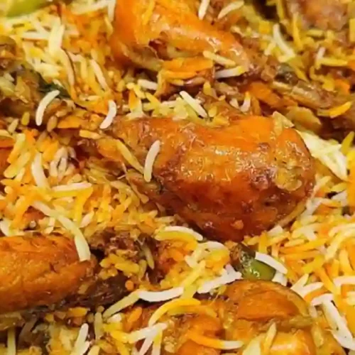 A close-up view of a pot filled with aromatic biryani, featuring golden pieces of chicken interspersed with vibrant, fluffy basmati rice garnished with orange and green spices.