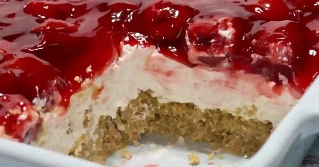 A close-up of a cheesecake topped with cherry glaze, showing a slice removed.