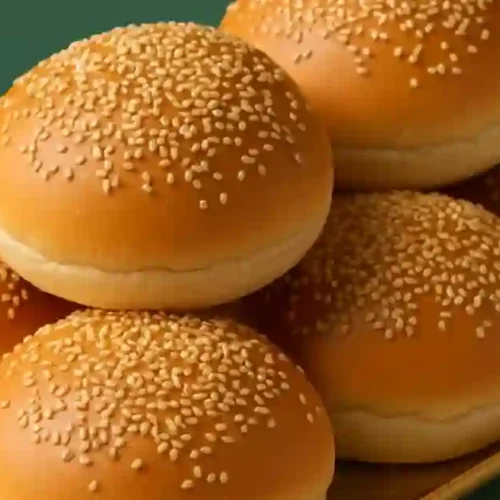 Six golden sesame seed buns stacked on a golden plate.