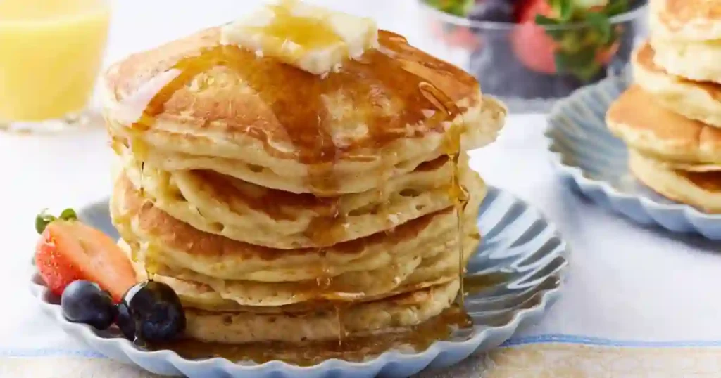 A mouthwatering stack of fluffy pancakes topped with melting butter and drizzled with syrup, served on a decorative plate.