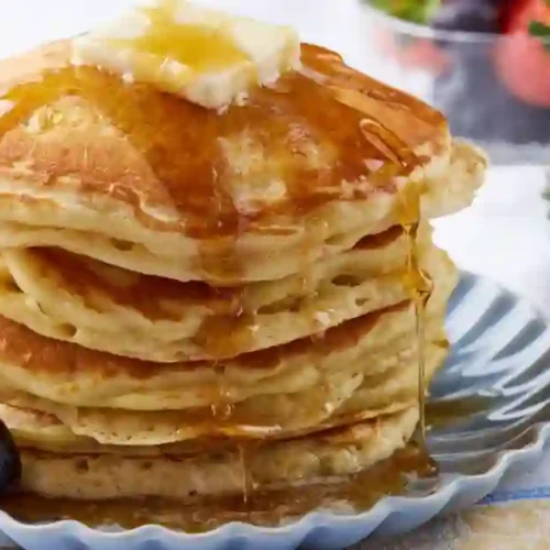 A mouthwatering stack of fluffy pancakes topped with melting butter and drizzled with syrup, served on a decorative plate.