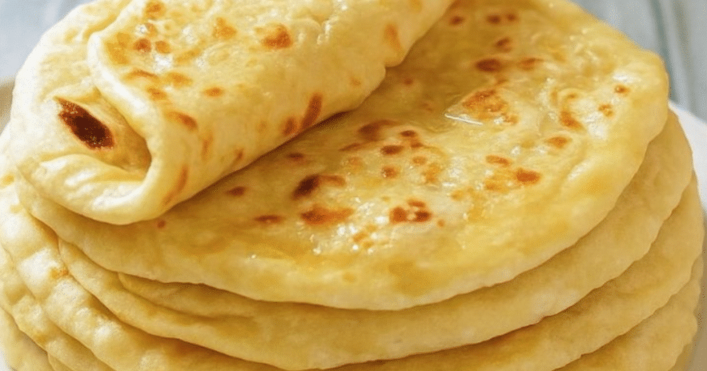 A stack of golden, soft Turkish flatbreads (Bazlama) with one bread folded on top, showcasing a slightly shiny surface and cooking marks.