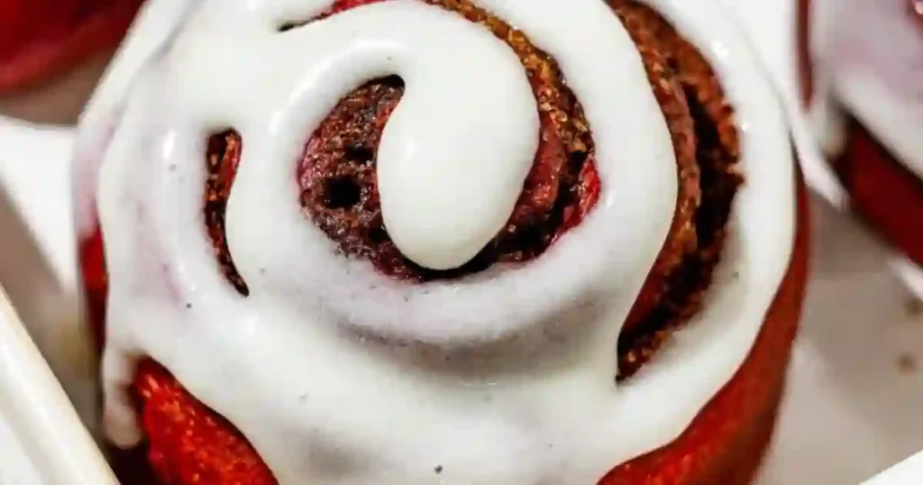 Close-up of a red velvet cinnamon roll topped with cream cheese frosting.