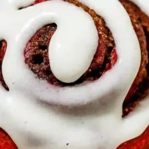 Close-up of a red velvet cinnamon roll topped with cream cheese frosting.