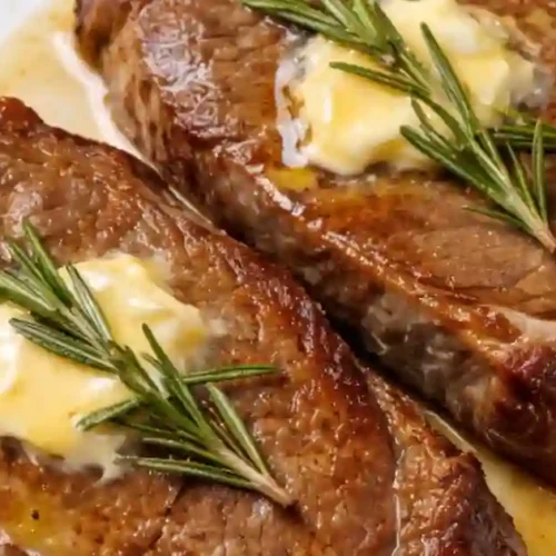 A perfectly cooked steak garnished with garlic butter and fresh herbs, resting on a white plate.