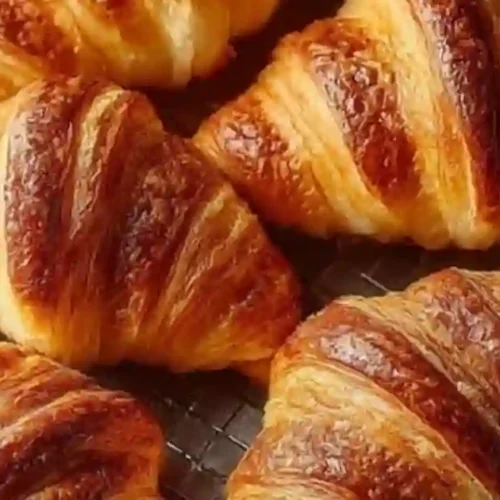 Freshly baked golden croissants arranged on a cooling rack, showcasing their flaky layers.