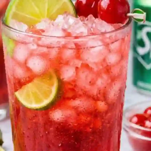 A close-up of a glass of cherry limeade with crushed ice, garnished with lime slices and maraschino cherries, with a Sprite can in the background.