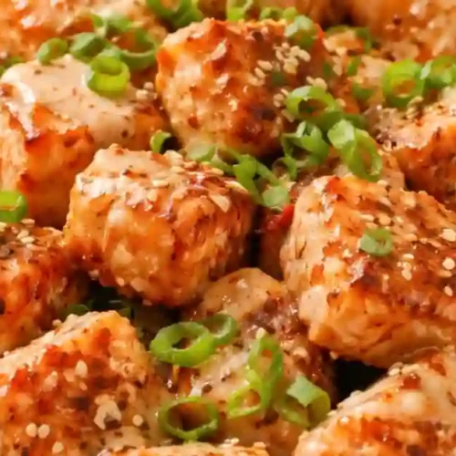 Delicious crispy salmon bites topped with green onions and sesame seeds in a white bowl.