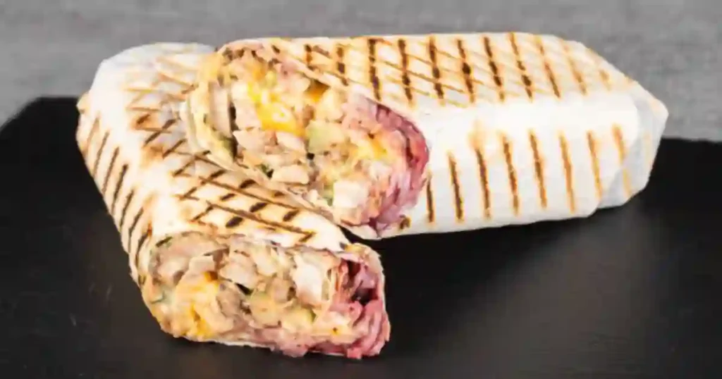 Two grilled BLT wraps, cut in half, showcasing crispy bacon, lettuce, and tomato filling.