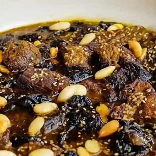 A traditional Moroccan beef tagine featuring tender beef pieces, prunes, and topped with sesame seeds and almonds, all simmering in rich spices.