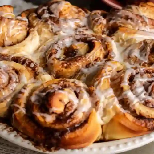 A beautifully arranged plate of soft and fluffy cinnamon rolls drizzled with white icing, showcasing their swirled layers and rich cinnamon filling.