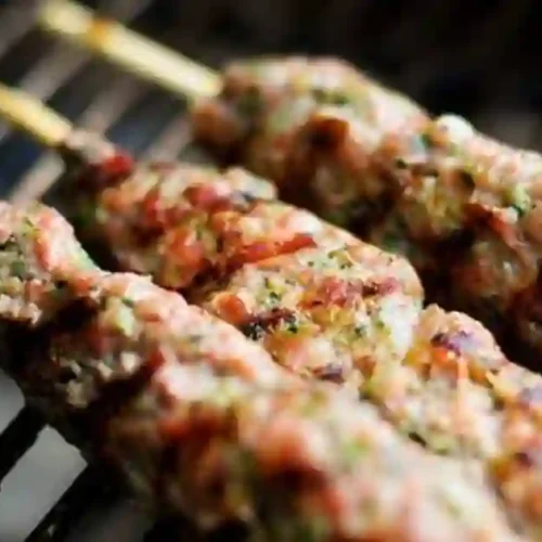 Grilled Lebanese kafta skewers sizzling on a grill, showcasing juicy meat mixed with herbs and spices.
